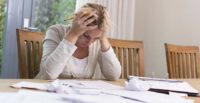 Woman looking distressed at papers spread out over a table, with her elbows on the table and her hands on either side of her forehead