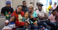 Immigrants from Haiti listen to someone speaking as they sit at a hotel in chairs with luggage around them