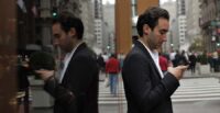 A man types on his mobile phone against a polished surface that shows his reflection