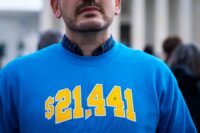 An image of a man's lower part of his face and chest as he wears a blue sweatshirt with "$21,441" printed on it in yellow